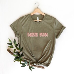 May include: A green t-shirt with the text "DOBIE MOM" in pink outlined letters.