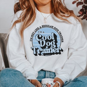 May include: White sweatshirt with a blue and white retro design that says "I'm not like a regular dog trainer, I'm a Cool Dog Trainer".