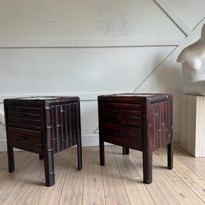 May include: Two dark brown bamboo nightstands with two drawers each. The nightstands have a square shape and are made of vertical bamboo slats. A white sculpture sits on a light-colored square pedestal.