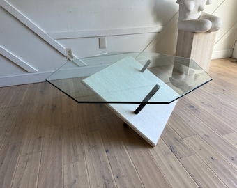 May include: Modern octagonal glass coffee table with a white and gray geometric base and black metal supports. The table is a unique design element for a living room.