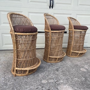 May include: Three wicker bar stools with brown cushions. The stools are made of natural woven wicker and have a rounded back.
