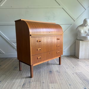 May include: A mid-century modern wooden desk with a curved top and three drawers. The desk is made of light brown wood and has a minimalist design. The desk is supported by four slender legs.