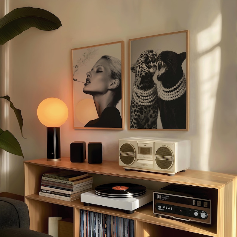 May include: A modern living room setup featuring a wooden shelf with a record player, stereo, and a vintage boombox. Two framed black and white art prints hang on the wall. A stylish lamp with a round, orange-yellow globe sits on the shelf.