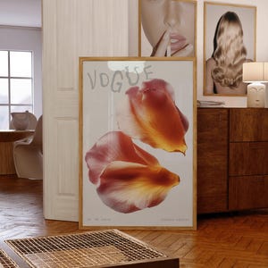May include: A framed print featuring two large, abstract flower petals in shades of orange and pink. The word "VOGUE" is at the top, with "no '26 issue" and "limited edition" at the bottom. The print is displayed in a room with other framed art.
