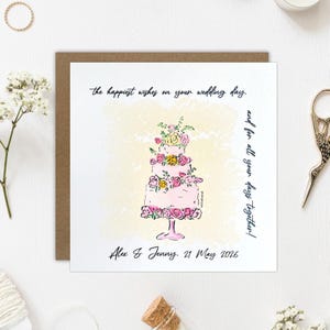 Könnte beinhalten: Eine quadratische Hochzeitsgrußkarte mit einer handgezeichneten Illustration einer dreistöckigen rosa Torte, die mit bunten Blumen auf einem Ständer verziert ist. Der Text lautet: the happiest wishes on your wedding day, and for all your days together! Alex & Jenny. 21 May 2026.