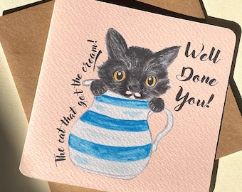 May include: A square greeting card with a pink background features a black cat peeking out of a blue and white striped teacup. The text reads "The cat that got the cream!" and "Well Done You!"