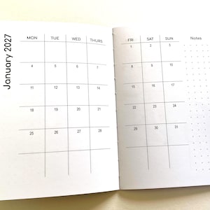 May include: An open planner showing a monthly calendar for January 2027. The left page displays days Monday through Thursday, while the right page shows Friday through Sunday with a dotted notes column. The layout features black grid lines.