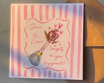 May include: Pink and white striped card with a champagne bottle popping open with pink hearts and glitter. The card says "Jane & Liam Congrats on your Engagement!"