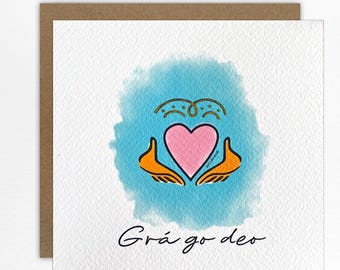 May include: A square greeting card featuring a watercolour blue background with a pink heart held by two orange hands. Above the heart is a gold decorative line, and below the illustration is the black text Grá go deo in a cursive script.
