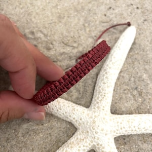 May include: A close-up of a maroon braided bracelet on a white starfish background.
