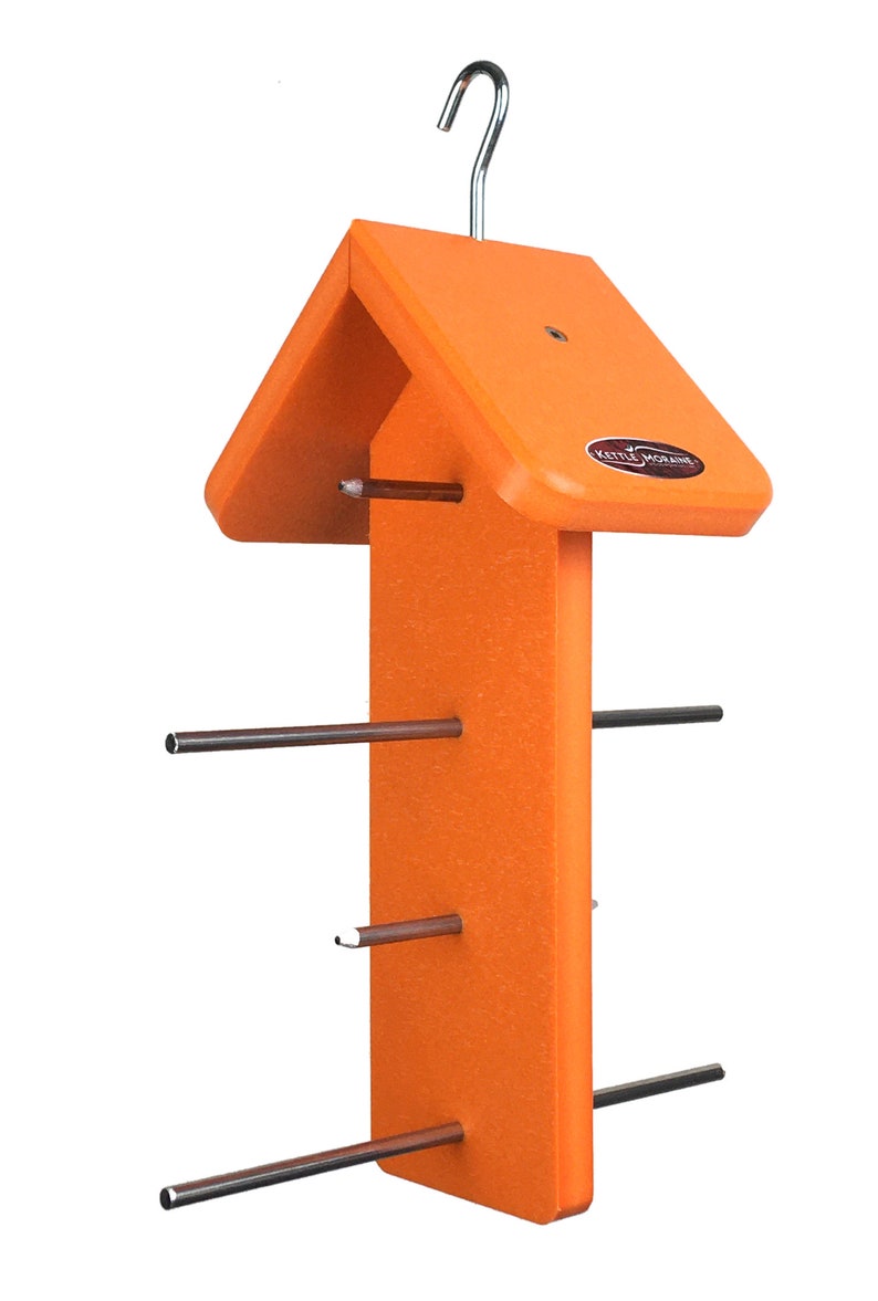 Puede incluir: Un comedero para p&aacute;jaros naranja con techo a dos aguas y un gancho met&aacute;lico para colgar. El comedero tiene varias varillas met&aacute;licas que se extienden desde la estructura central, dise&ntilde;adas para sujetar comida para p&aacute;jaros. La marca "Kettle Moraine" es visible.