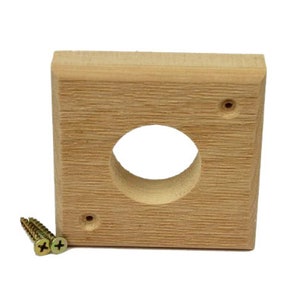 May include: A square wooden block with a round hole in the center. There are two screws on the top and one on the side. The block is light brown in color.