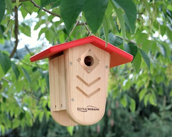 Könnte beinhalten: Ein Vogelhaus aus Holz mit einem roten Dach und einem kupfernen Einflugloch. Das Vogelhaus hat ein einzigartiges Design mit einer abgerundeten Vorderseite und der Aufschrift "Kettle Moraine".