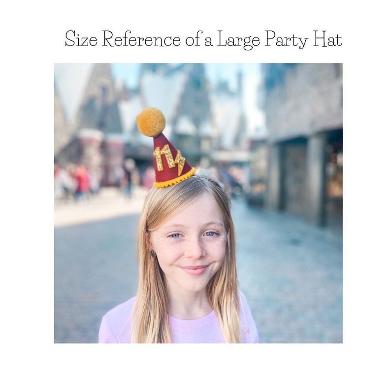 May include: A red and gold party hat with a lightning bolt design and a yellow pom-pom on top. The hat is worn by a young person with blonde hair.