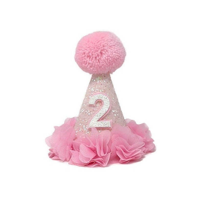 May include: Pink and white glitter party hat with a fluffy pom pom on top and the number 2 in silver glitter. The hat has a pink tulle ruffle around the bottom.