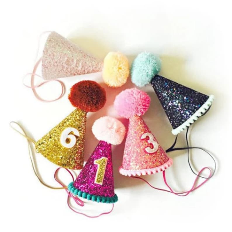 May include: Six colorful glitter party hats with pom poms and numbers 1, 3, and 6.