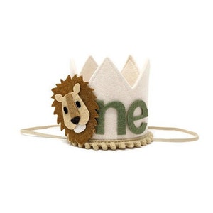 May include: A white felt crown with a green felt "one" and a brown felt lion face. The crown has a tan felt trim and a tan elastic band.