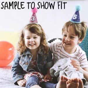 May include: Two children wearing birthday hats. The girl is wearing a pink hat with the number 3 on it. The boy is wearing a blue hat with the number 5 on it.