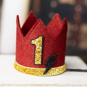 May include: Red felt crown with a gold glitter number one and a black lightning bolt. The crown has a gold glitter trim.