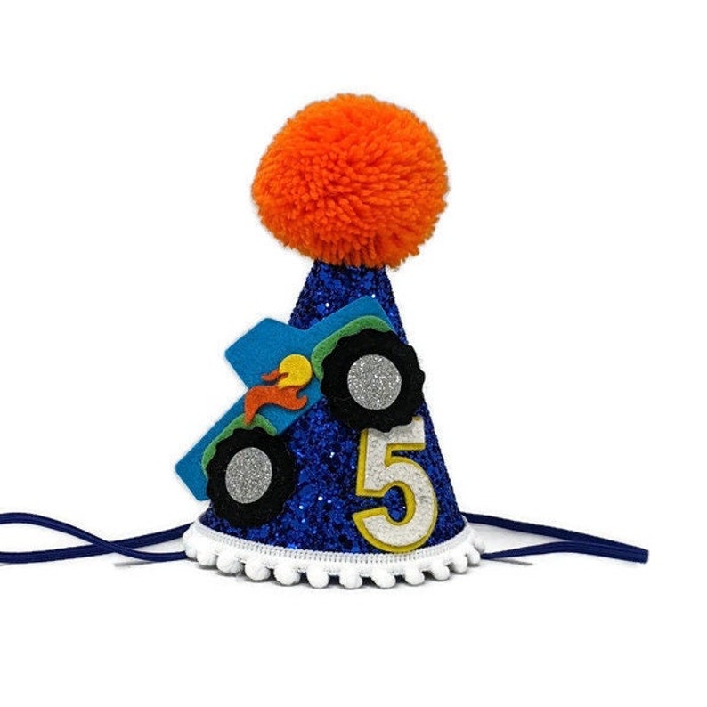 Op de afbeelding: Blauwe glitter-partyhoed met een monstertruck-ontwerp en het nummer 5. De hoed heeft een witte pompon-bies en een oranje pompon bovenop.