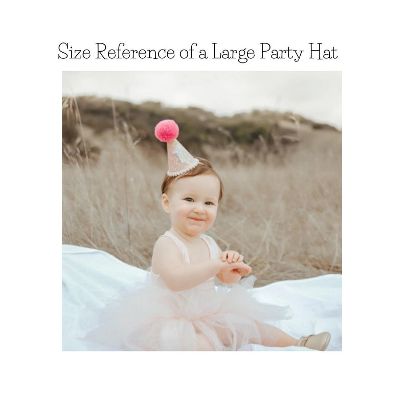 May include: A pink and white party hat with a pink pom-pom on top. The hat is worn by a young child sitting on a white blanket.