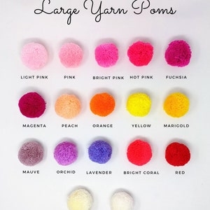 May include: A collection of large yarn pom-poms in various colors, including light pink, pink, bright pink, hot pink, fuchsia, magenta, peach, orange, yellow, marigold, mauve, orchid, lavender, bright coral, red, cream, and white.