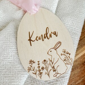 May include: A wooden Easter egg ornament with the name "Kendra" engraved on it. The ornament features a bunny rabbit and floral designs.