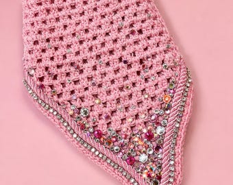 Könnte beinhalten: Ein rosa gehäkeltes Accessoire mit dekorativem Rand und verziert mit Strasssteinen und Perlen. Es hat eine schwarze Schnur. Der Hintergrund ist einfarbig rosa.