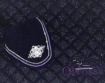 May include: A navy blue equestrian saddle pad with a quilted pattern and sparkling glitter. The pad features a decorative crystal and rhinestone design, with a purple and silver trim. The Olvossa logo is embroidered in purple.