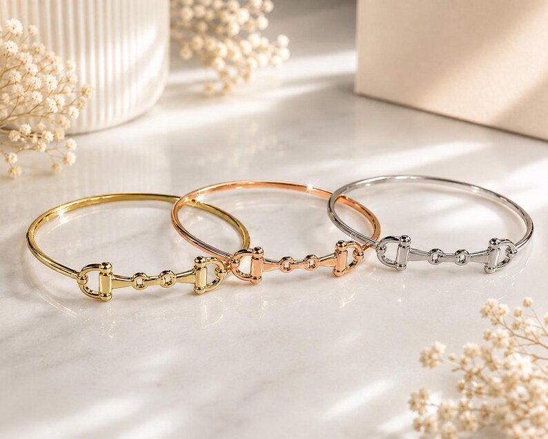 May include: Three metal bangle bracelets featuring a horse bit design. The set includes one gold-tone, one rose gold-tone, and one silver-tone bracelet, each with a polished finish and a central equestrian-inspired link detail.