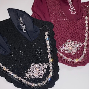 May include: Two horse ear bonnets, one black and one claret. Both are adorned with rhinestones and pearl detailing. The ear covers have the word "Ofrossa" embroidered on them. The bonnets are designed for equestrian use.