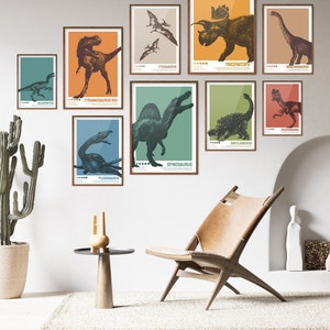 May include: A set of nine colourful dinosaur posters with illustrations of different dinosaurs, including Tyrannosaurus Rex, Triceratops, Velociraptor, and Spinosaurus. The posters are framed and hung on a white wall.