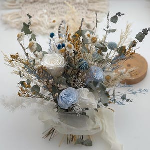 May include: A bouquet of dried flowers with white and blue roses, white and blue wildflowers, and dried grasses. The bouquet is tied with a white ribbon.