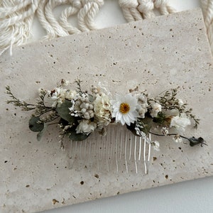 Puede incluir: Un peine para el cabello floral blanco y verde con un peine plateado. El peine está decorado con flores blancas secas y vegetación.