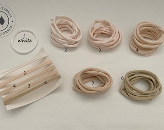 May include: Six different colors of fabric hair ties, labeled 1-6. The colors are white, light pink, darker pink, beige, light brown, and olive green. The hair ties are arranged in two rows on a white surface. The first row has three hair ties, and the second row has three hair ties.