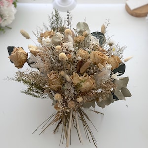 May include: A dried flower bouquet with beige and white flowers, dried grasses, and eucalyptus leaves.