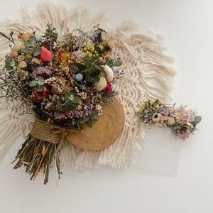 May include: A dried flower bouquet with a variety of colors, including pink, purple, blue, yellow, and green. The bouquet is tied with twine and is sitting on a white crocheted rug.