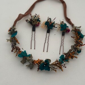 Puede incluir: Un conjunto de accesorios para el cabello con flores que incluye una corona de flores secas y tres horquillas a juego. La corona y las horquillas están adornadas con flores de color turquesa, naranja y blanco, con una cinta marrón.