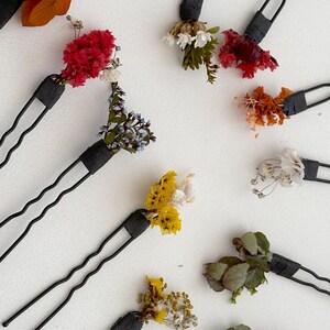 Puede incluir: Surtido de diez pinzas para el pelo con flores secas. Las flores son de varios colores, incluyendo rojo, naranja, amarillo, blanco y verde. Las pinzas son negras y tienen un diseño sencillo.