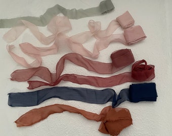 Puede incluir: Surtido de ocho cintas de seda en varios colores, incluyendo verde salvia, rosa rubor, burdeos, azul marino y naranja óxido. Las cintas están dispuestas sobre una superficie blanca.