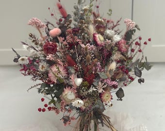 Könnte beinhalten: Ein großer Strauß getrockneter Blumen in Rosa-, Rot- und Weißtönen. Das Arrangement umfasst verschiedene Texturen und Formen, mit Beeren und Grün. Die Stiele sind mit Bindfaden zusammengebunden, was einen rustikalen und natürlichen Look erzeugt.