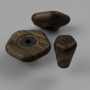 Könnte beinhalten: Drei dunkelbraune Holzknöpfe mit sichtbarer Holzmaserung. Ein Knopf ist flach und sechseckig mit einem schwarzen quadratischen Mittelloch, während die anderen beiden abgerundet und kegelförmig sind und konzentrische Ringe an der Oberseite zeigen.
