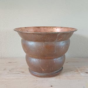 May include: A copper planter with a flared rim and a wavy, textured design. The planter has a worn, aged look.