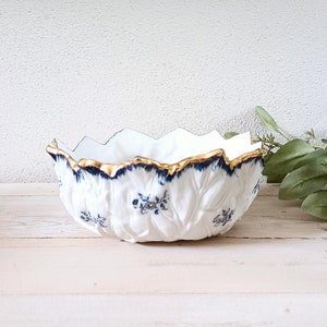 May include: A white ceramic bowl with a blue and gold floral design. The bowl is shaped like a flower and has a scalloped edge.
