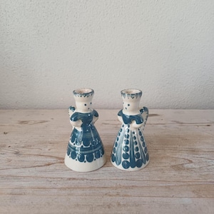 May include: Two ceramic angel figurines. The angels have white bodies with blue dresses and wings. The dresses are decorated with a dotted pattern. The angels have a crown-like design on their heads.