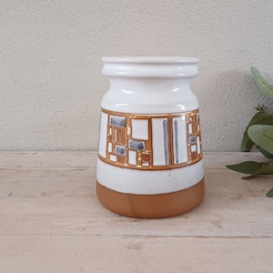 May include: A white ceramic vase with a geometric pattern in brown and grey. The vase has a rounded base and a wide opening.