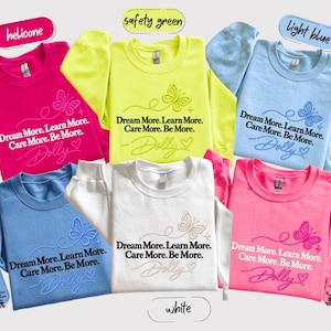 A collage of six colorful t-shirts with the same design, featuring the text "Dream More. Learn More. Care More. Be More." printed on them.
