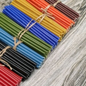 May include: A bundle of colourful beeswax candle wicks, tied together with twine. The wicks are arranged in a rainbow pattern, starting with brown, orange, yellow, blue, green, light blue, black, and red.