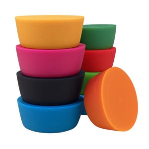 Könnte beinhalten: Eine Sammlung farbenfroher Silikon-Flaschenverschlüsse in verschiedenen Farbtönen. Die Verschlüsse sind gestapelt und angeordnet und zeigen eine Reihe von Farben, darunter Gelb, Pink, Schwarz, Blau, Grün, Rot und Orange. Die Verschlüsse sind zylindrisch mit flacher Oberseite.