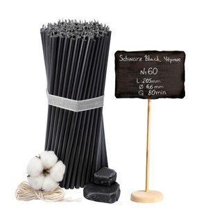 Könnte beinhalten: Ein Bündel mit 60 schwarzen Kerzen, jede 20,5 cm lang und 6,6 mm im Durchmesser. Die Kerzen sind mit einem weißen Band zusammengebunden. Ein kleines Schild aus Schiefertafel steht daneben und zeigt "Schwarz Black Черные N.60 L:205mm Ø 66 mm 80min".